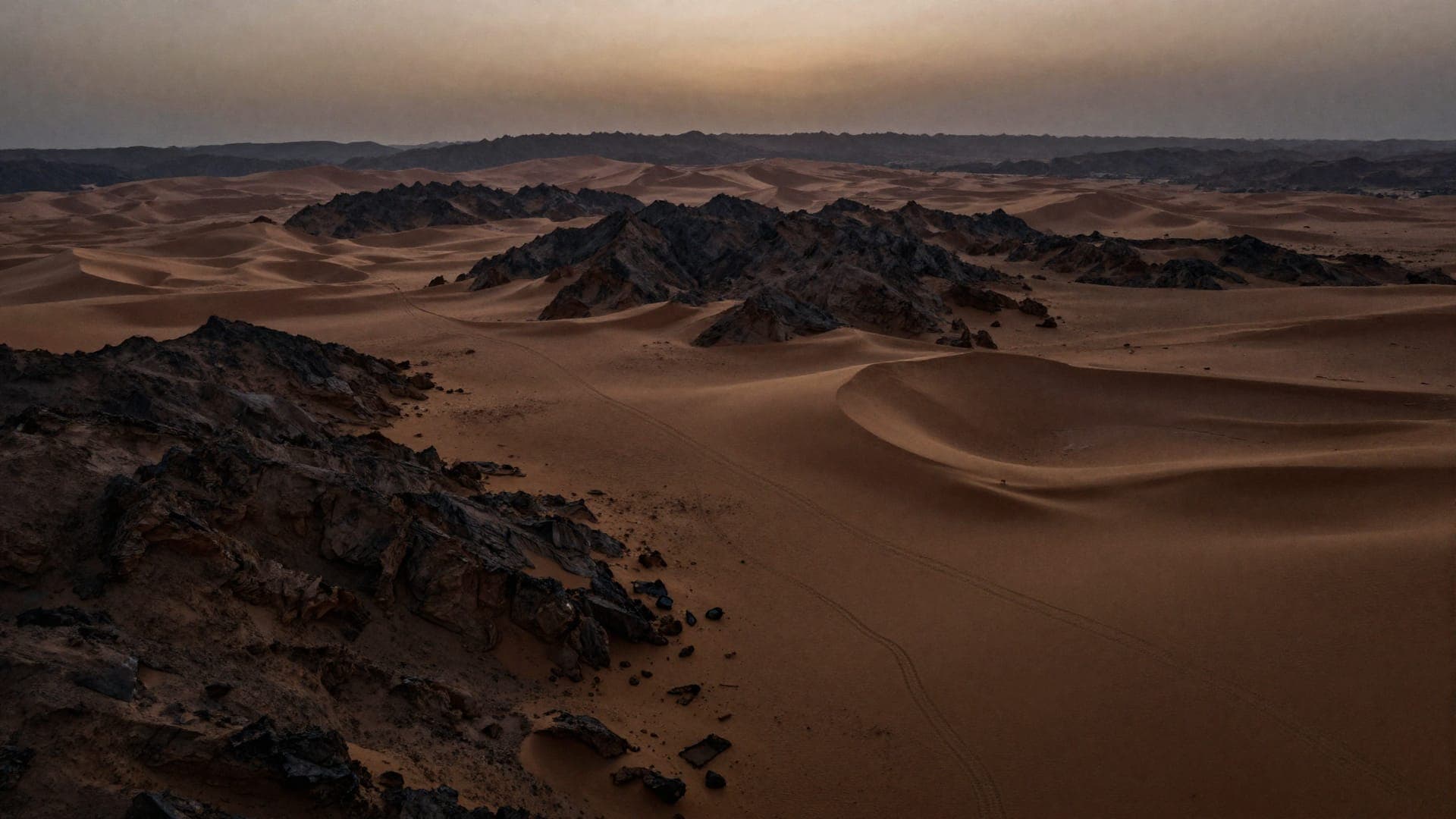 Wind-carved dunes running to a horizon of black volcanic rock, with a single vehicle track crossing the sand.